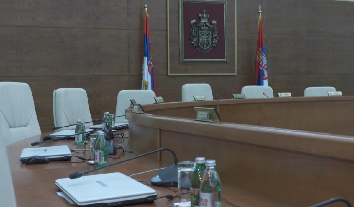 Prazna sala Ustavnog suda Srbije sa zastavama, grbom, mikrofonima i belim stolicama.