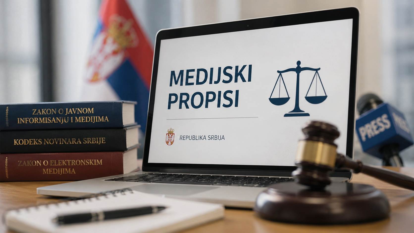 Laptop sa prikazom medijskih propisa pored zakonskih knjiga, mikrofona, sudijskog čekića i zastave Srbije.