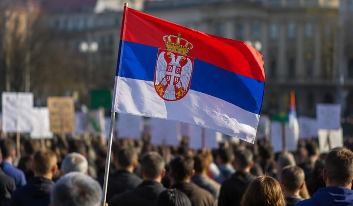 Zastava Srbije ispred okupljenih građana na javnom skupu u gradu.